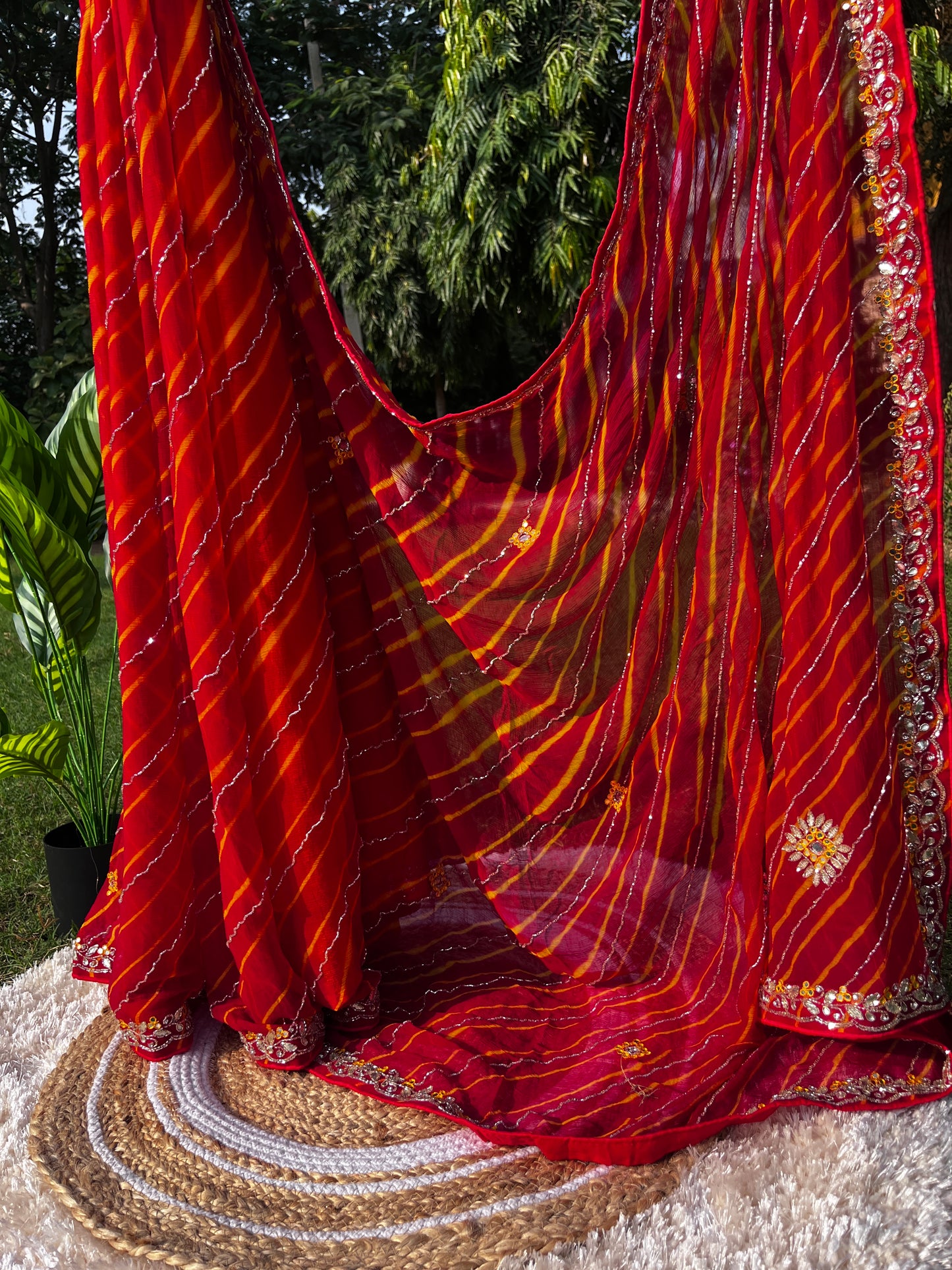 Vibrant Red Lehariya Pure Chiffon Saree featuring Heavy Kardhana and Gotta Patti Butta Work. Traditional Rajasthani handwork for wedding and festive wear. Saree plates hanging with the Rich and heavy Pallu of the saree