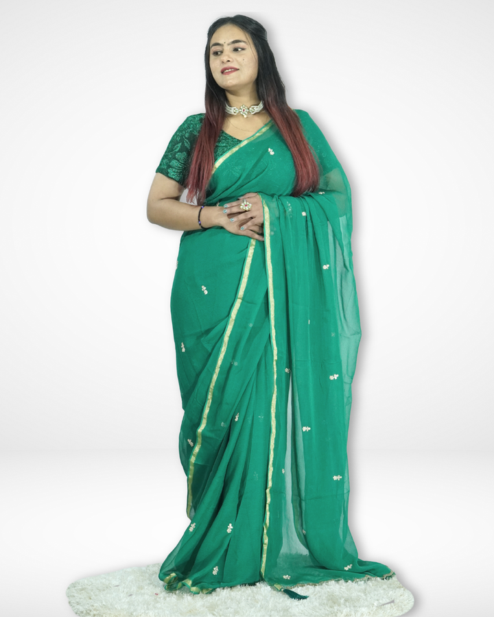 Model wearing an elegant emerald green chiffon saree with delicate zari buti work and a subtle gold border, styled with a matching blouse, showcasing Amai Jaipur’s lightweight festive and occasion wear saree collection.