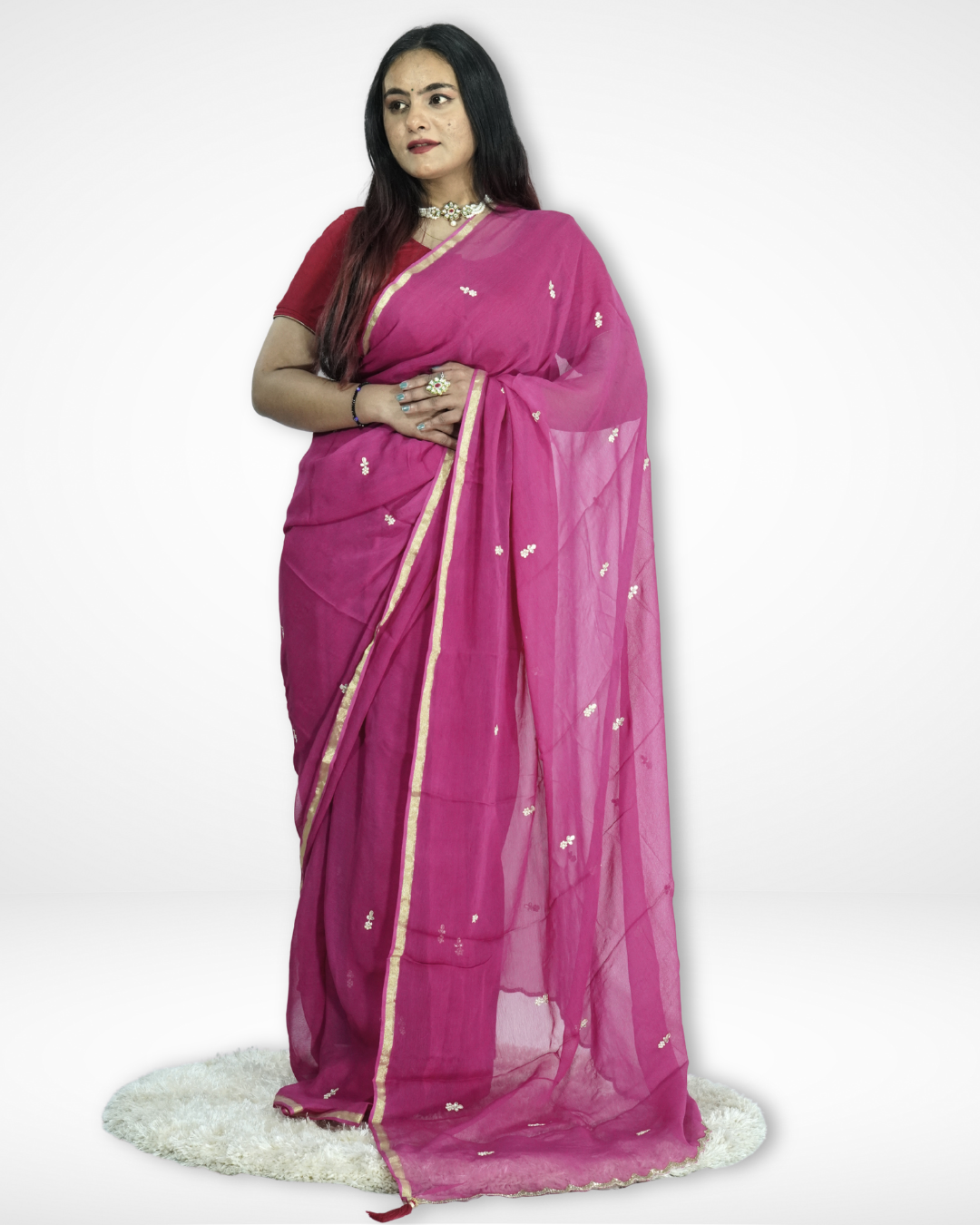 Model wearing a vibrant rani pink chiffon saree featuring delicate gold buti motifs and a refined gold border, paired with a matching blouse and statement jewelry for an elegant festive look by Amai Jaipur. ✨