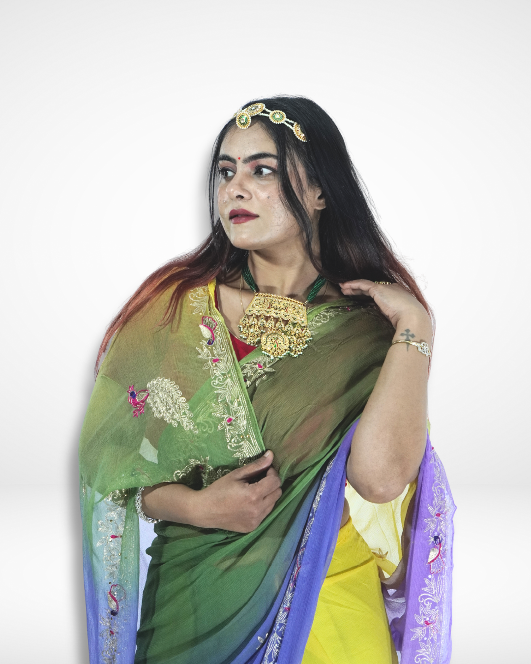 Close-up portrait of a woman wearing a multicolored saree with green, blue, and yellow tones, adorned with delicate embroidery and styled with a statement gold necklace and headpiece. ✨