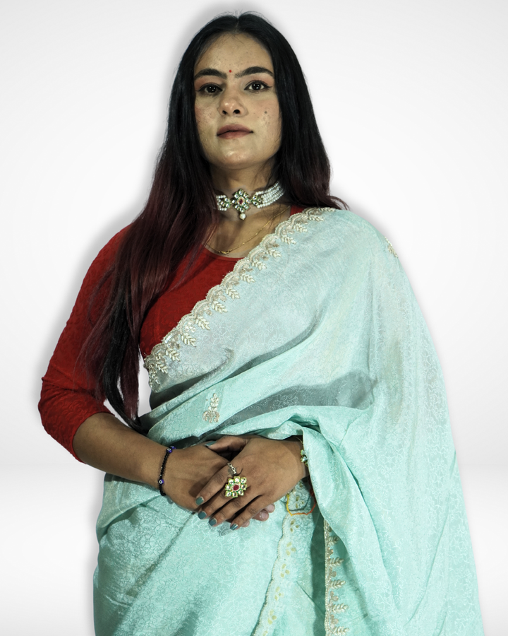 Woman wearing a mint green saree with delicate gold embroidered border and subtle woven patterns, paired with a red blouse and traditional jewelry, posing elegantly against a plain background. ✨