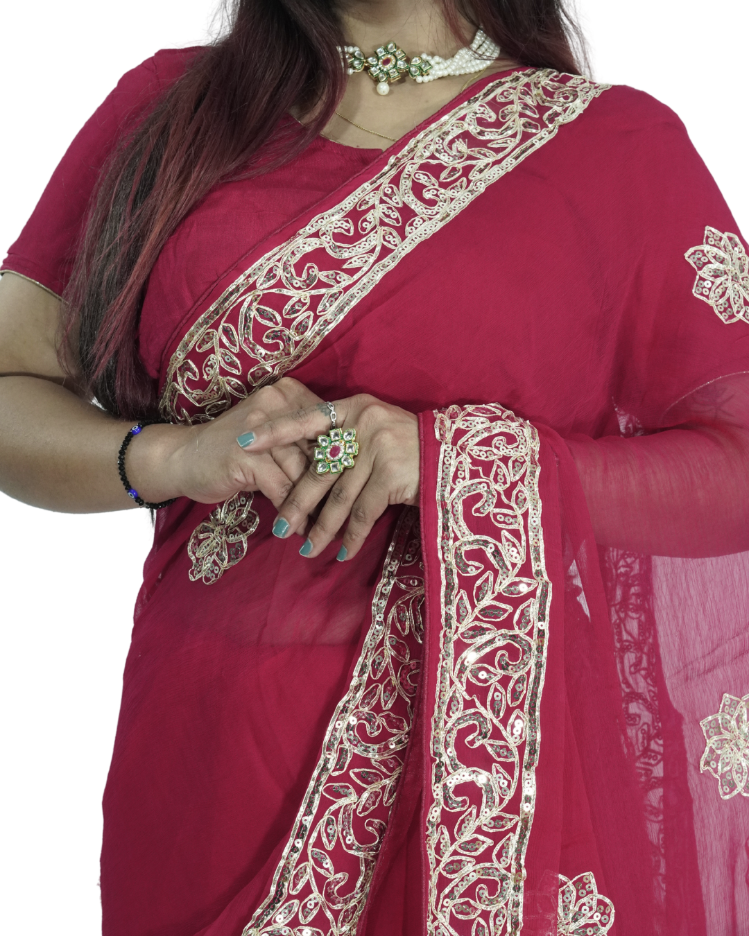 Close-up of a woman wearing a deep red saree with intricate gold embroidered vine border along the pallu, paired with a matching blouse and traditional jewelry, highlighting the detailed border work and elegant drape. ✨