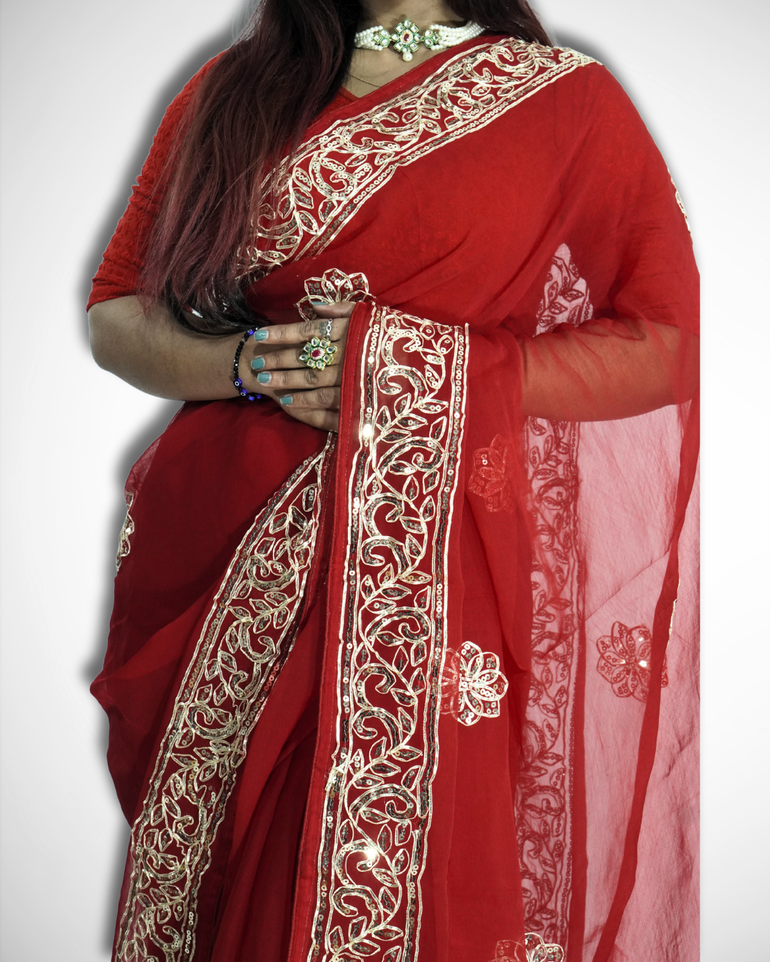 Close-up of a woman wearing a vibrant red saree with intricate gold embroidered vine border and delicate floral butta motifs, highlighting the sheer pallu and detailed craftsmanship paired with traditional jewelry. ✨