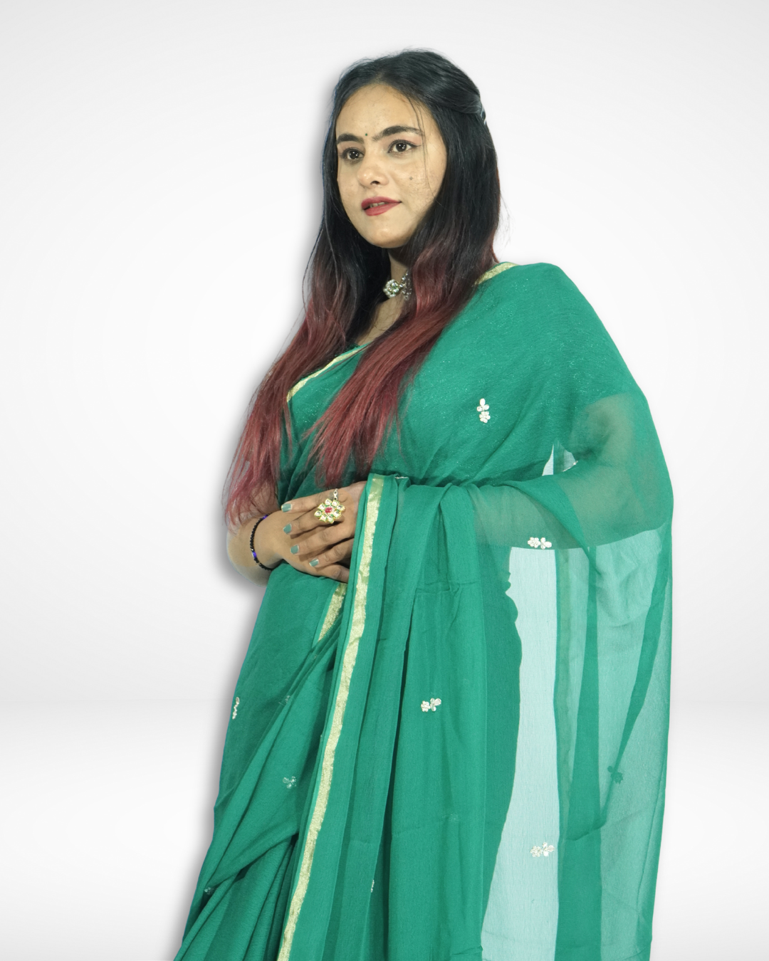 Model draped in a graceful emerald green chiffon saree featuring delicate floral buti work and a subtle gold border, paired with a matching blouse and statement jewelry for an elegant festive look by Amai Jaipur. ✨