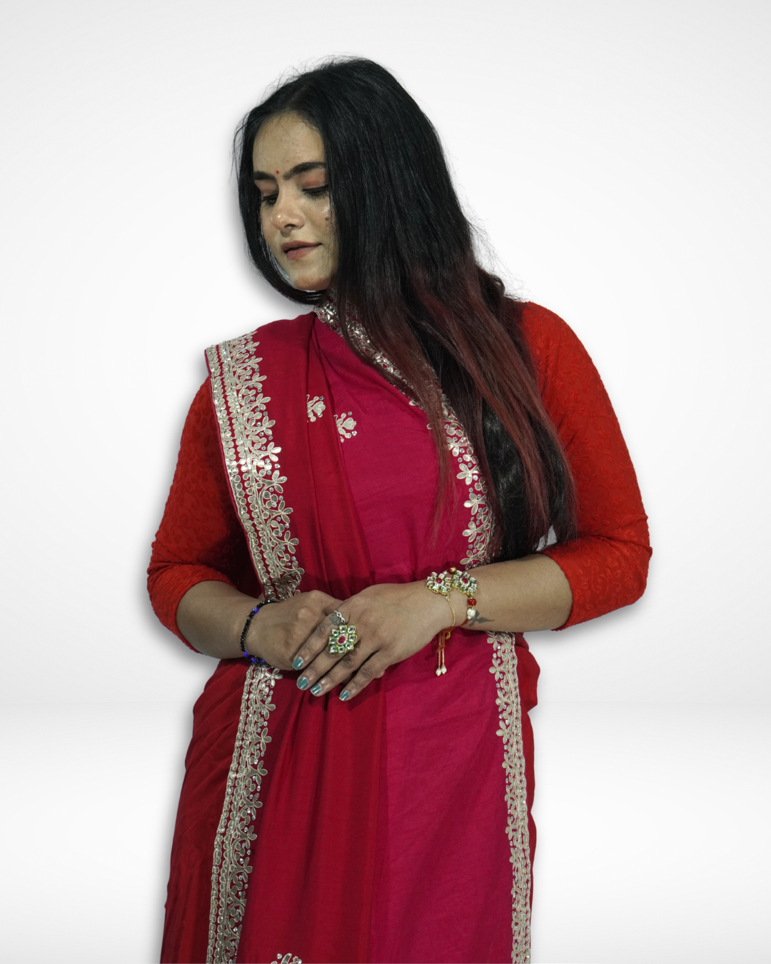 Woman wearing a red saree with intricate gold embroidered borders and motifs, styled with a matching red blouse and traditional jewelry, posing gracefully while looking down against a plain background. ✨