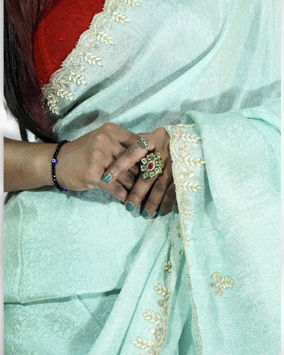 Close-up of a mint green saree highlighting delicate gold embroidered border and subtle woven patterns, with hands gently resting on the fabric showcasing traditional jewelry and craftsmanship details. ✨