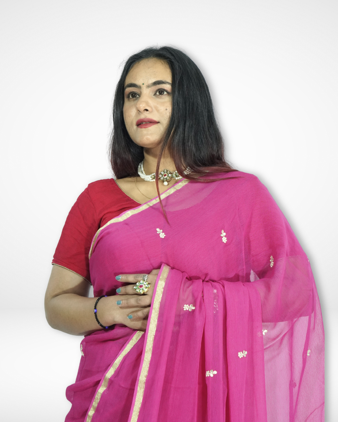 Model styled in a bright rani pink chiffon saree with delicate gold buti detailing and a subtle gold border, paired with a matching blouse and statement choker for an elegant festive look by Amai Jaipur. ✨