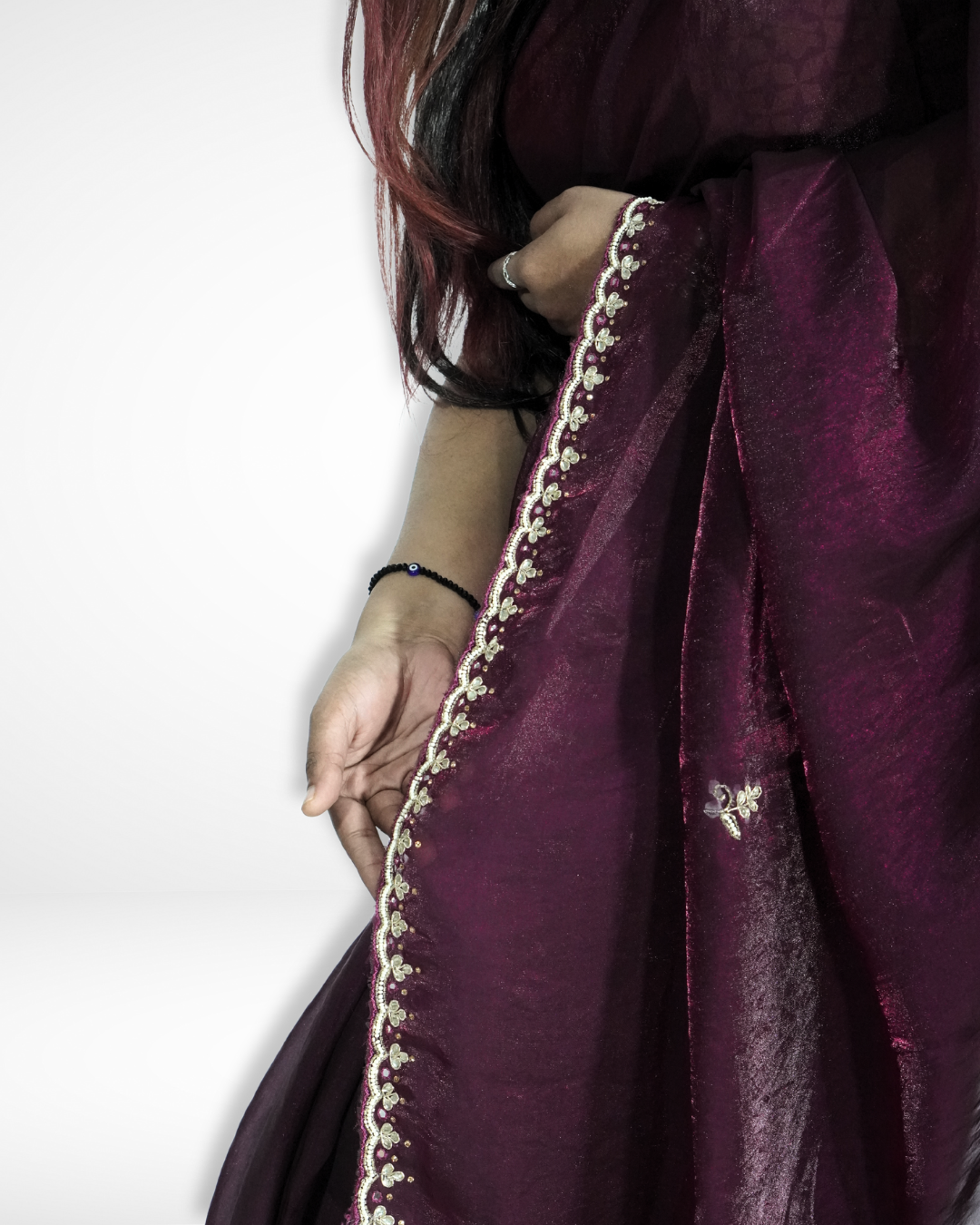 Close-up of a rich wine-purple saree highlighting its shimmering fabric, delicate floral embroidered border, and small scattered motifs, gracefully draped over the model’s arm. ✨