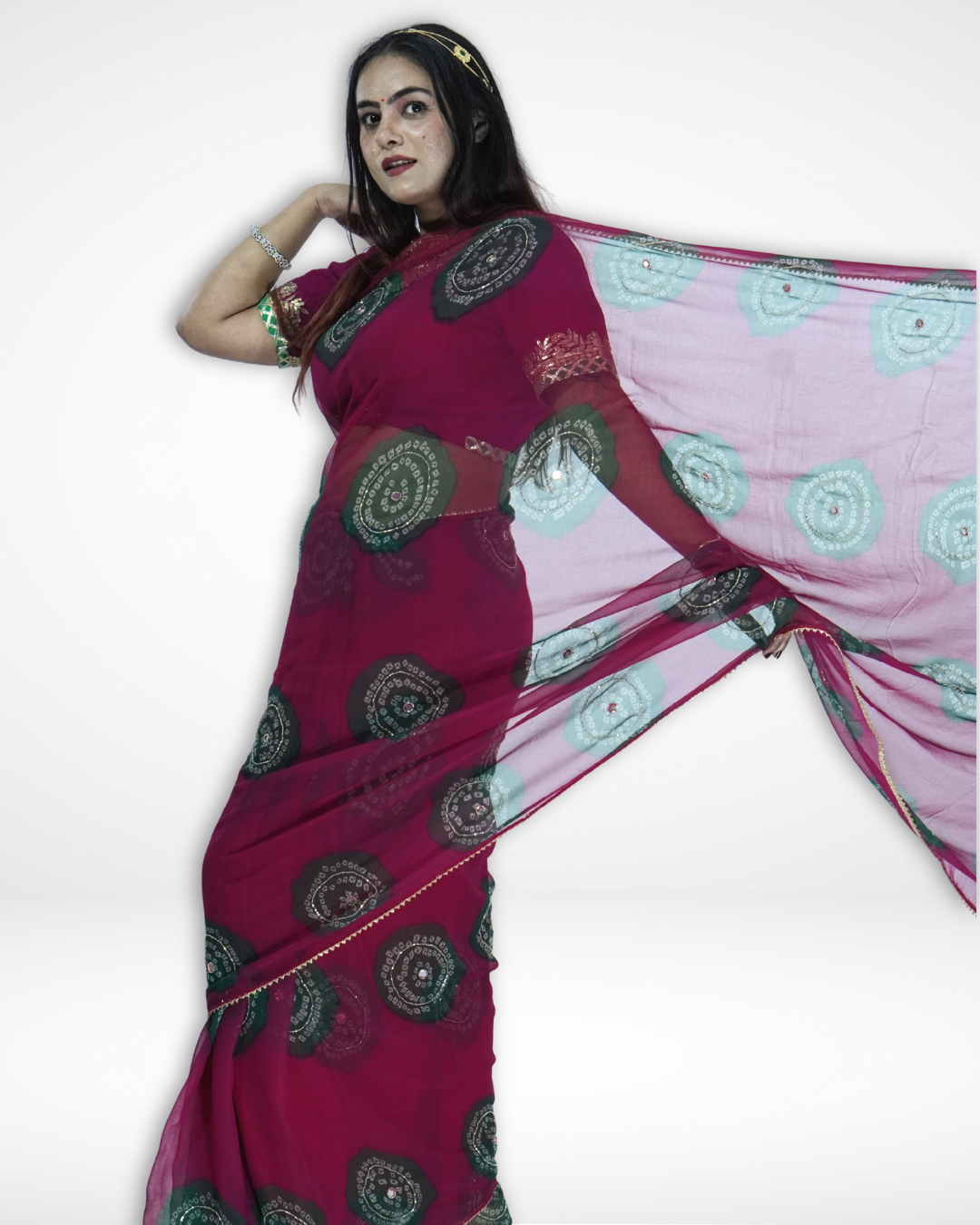 Model posing in a flowing deep magenta chiffon saree with green bandhani-style circular motifs, gracefully extending the pallu to showcase the lightweight fabric and elegant festive design by Amai Jaipur. ✨