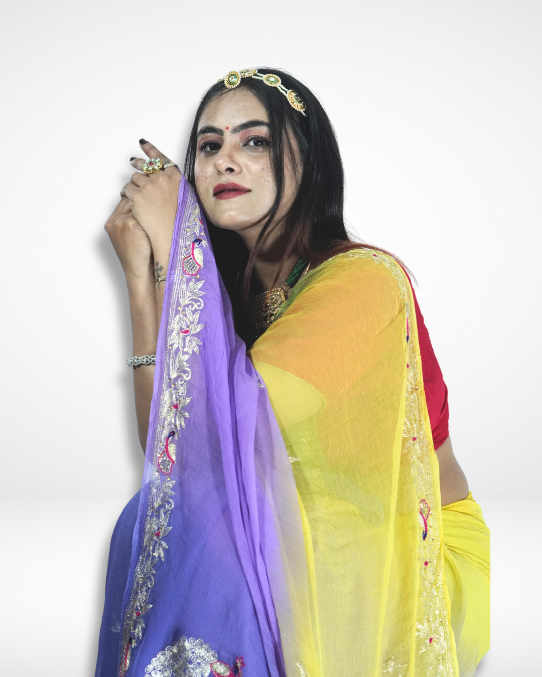 Close-up portrait of a woman draped in a multicolored saree with yellow, green, and purple gradient tones, featuring intricate embroidered borders, styled with a gold headpiece, statement necklace, and traditional jewelry. ✨
