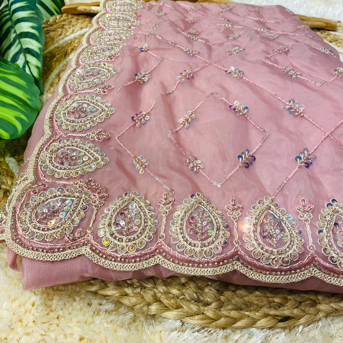 Blush pink saree spread over a woven jute mat, featuring an ornate paisley embroidered border with sequins and beadwork, complemented by delicate diamond-pattern threadwork and scattered sequin floral accents across the fabric. ✨