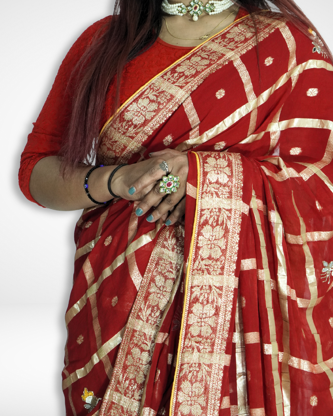 Close-up of a red saree featuring an elegant gold zari floral border and checkered pattern with delicate buti motifs, styled with traditional jewelry for a rich festive look. ✨