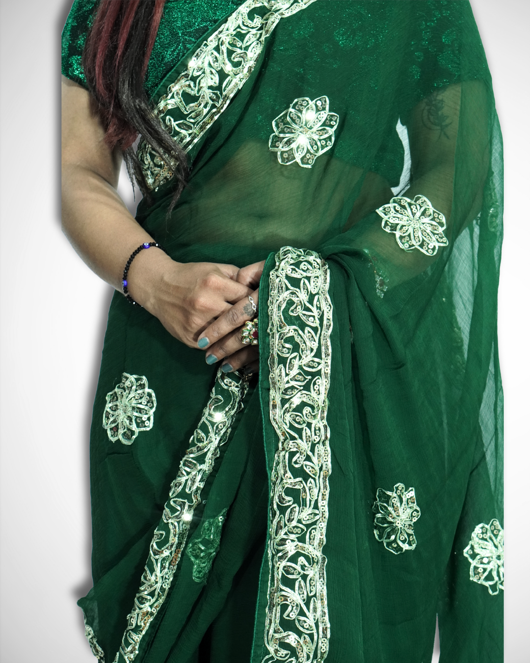 Close-up of a woman wearing a deep emerald green saree with intricate silver embroidered vine border and scattered floral butta motifs, highlighting the delicate sheer fabric and detailed craftsmanship. ✨