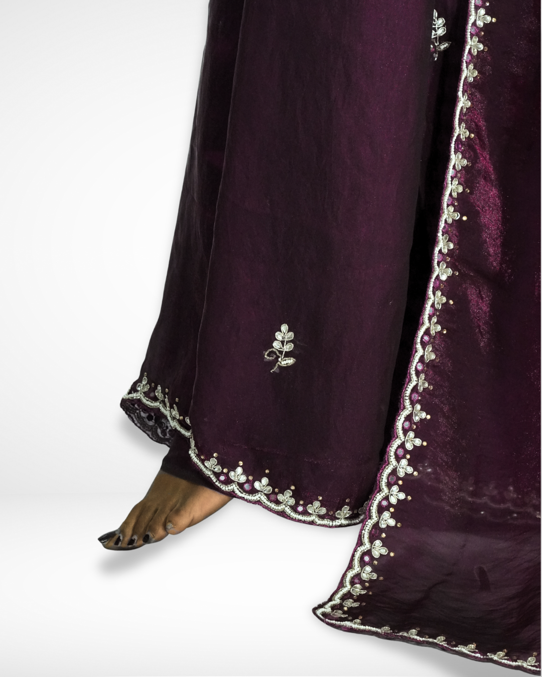 Close-up of the deep wine-purple saree hem featuring a delicate floral embroidered border and small leaf motifs, highlighting the elegant drape and fine detailing near the edge. ✨