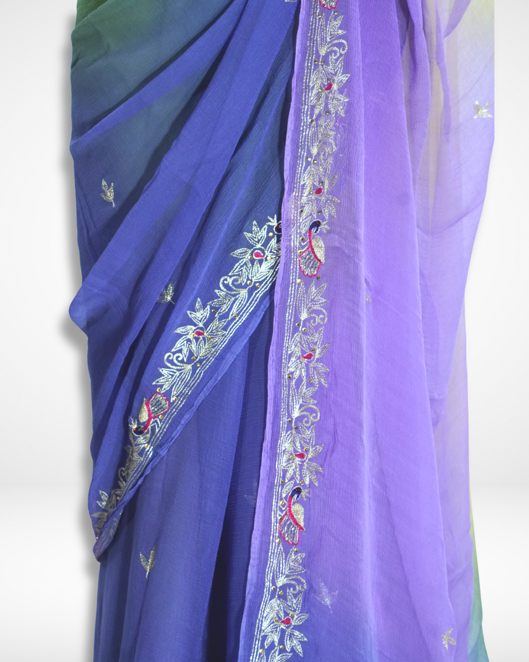 Close-up detail of a multicolor saree drape featuring purple and blue gradient fabric with intricate silver embroidery and peacock motifs along the border. ✨