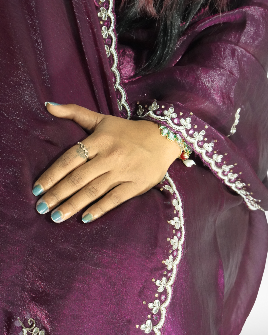 Close-up of a deep wine-purple saree showing its soft shimmer and delicate floral embroidered border, with the model’s hand resting gracefully on the drape highlighting the intricate detailing. ✨
