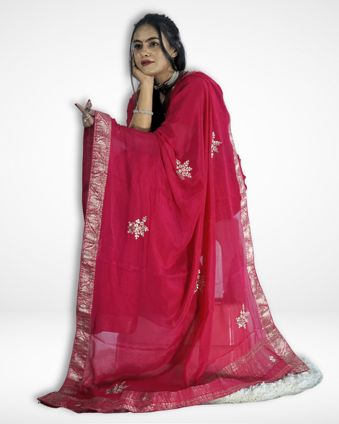 Model seated gracefully in a vibrant pink saree featuring an elegant silver zari border and delicate embroidered motifs, with the sheer pallu draped around to showcase its lightweight fabric and festive elegance. ✨