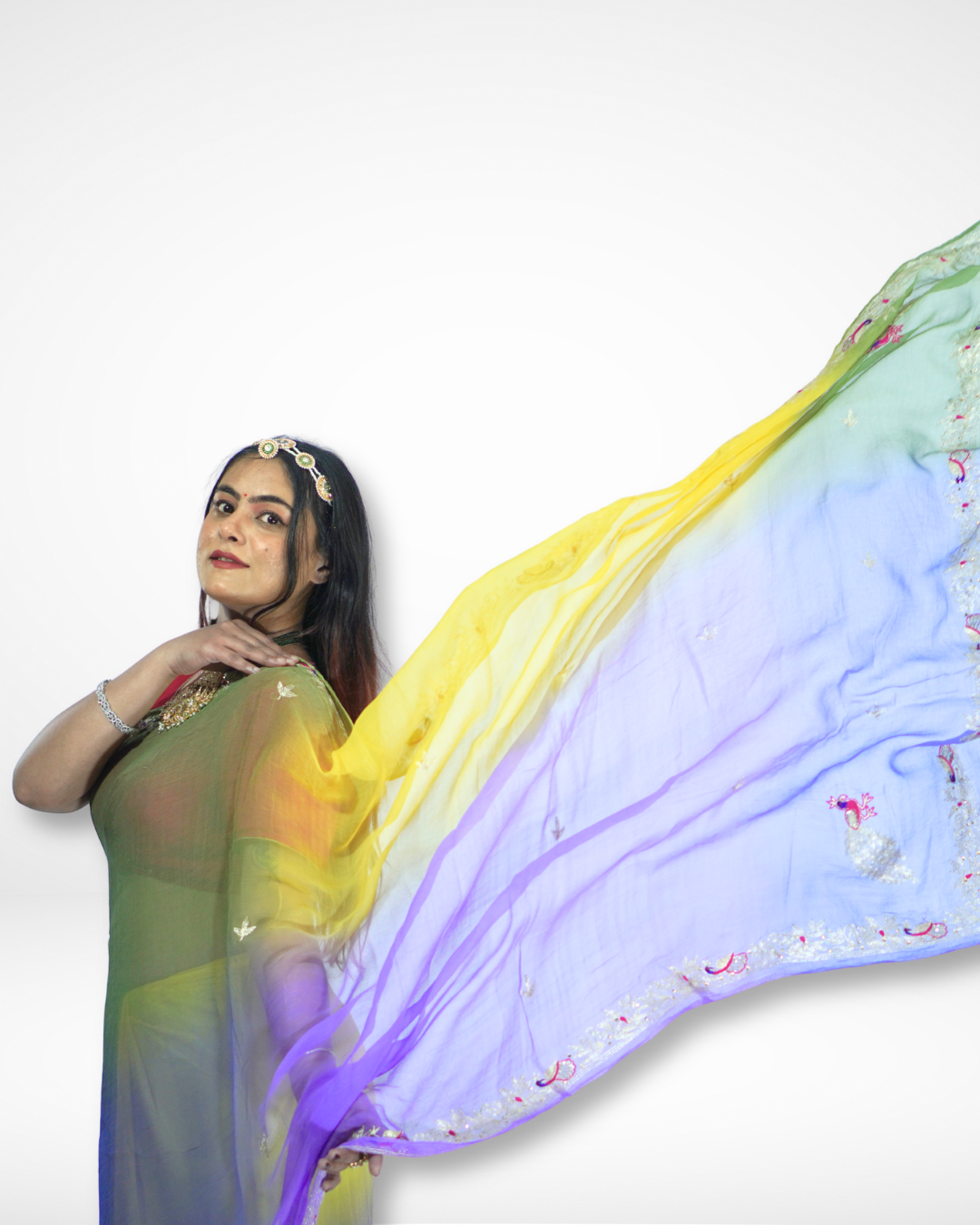 Woman posing gracefully in a flowing multicolor gradient saree with yellow, green, and purple hues, showcasing the lightweight drape and delicate embroidered border as the pallu extends elegantly in the air. ✨