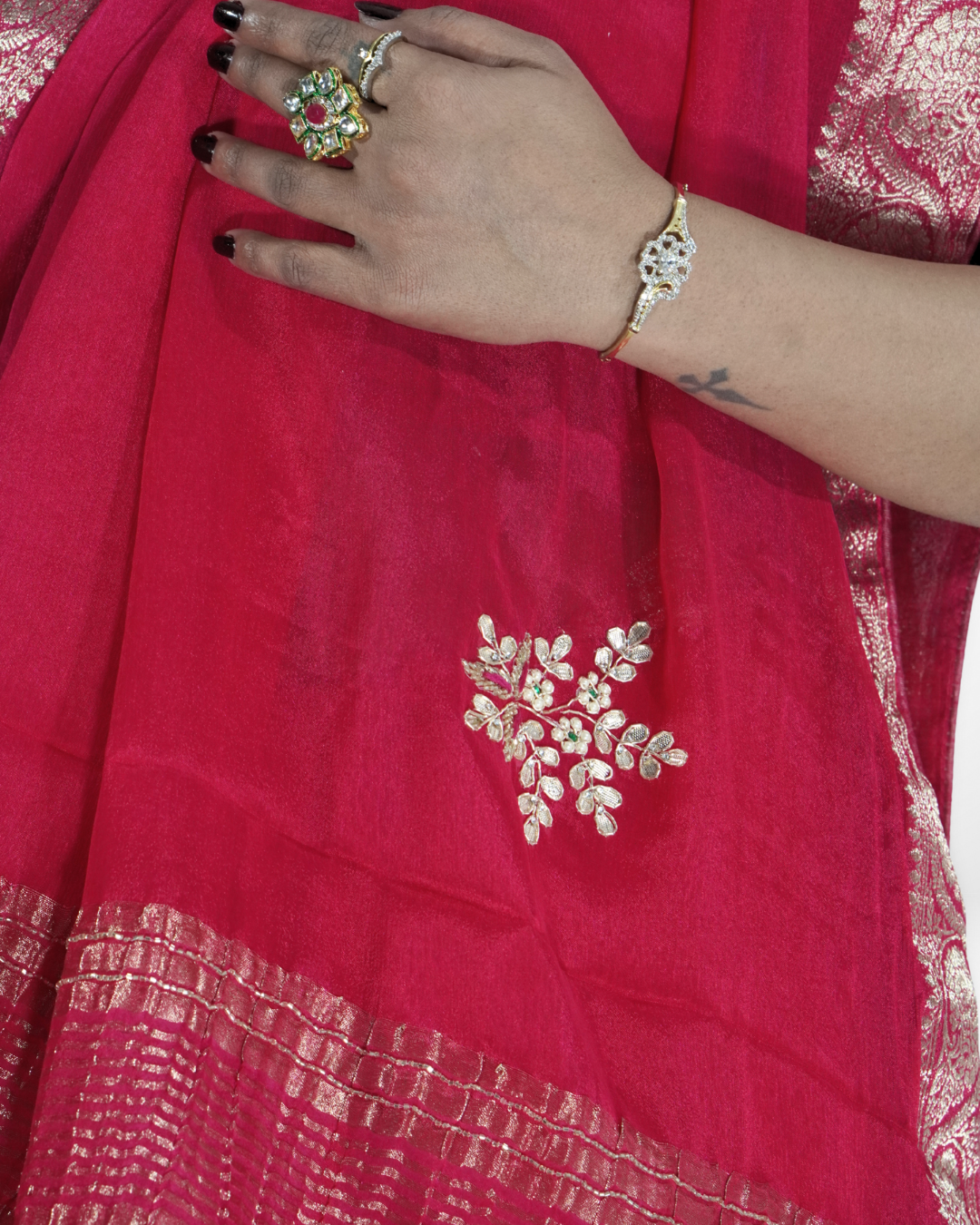 Close-up detail of a vibrant pink saree featuring a delicate silver embroidered floral motif and shimmering zari border, highlighted with traditional jewelry and elegant draping. ✨
