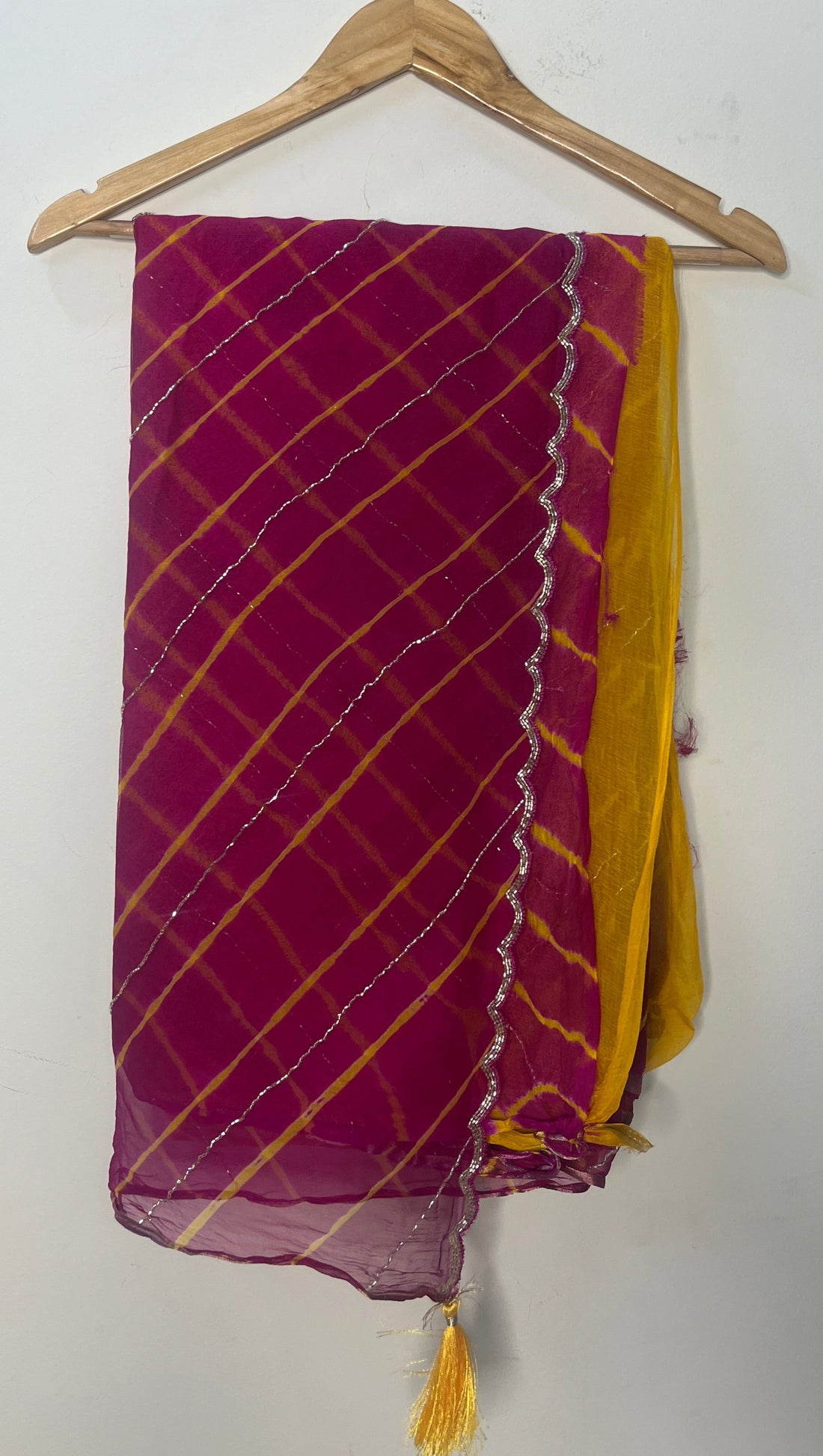 Magenta and pink tie-dye saree with diagonal yellow stripes and delicate silver shimmer lines, finished with a scalloped metallic border and mustard yellow pallu, displayed on a wooden hanger. ✨