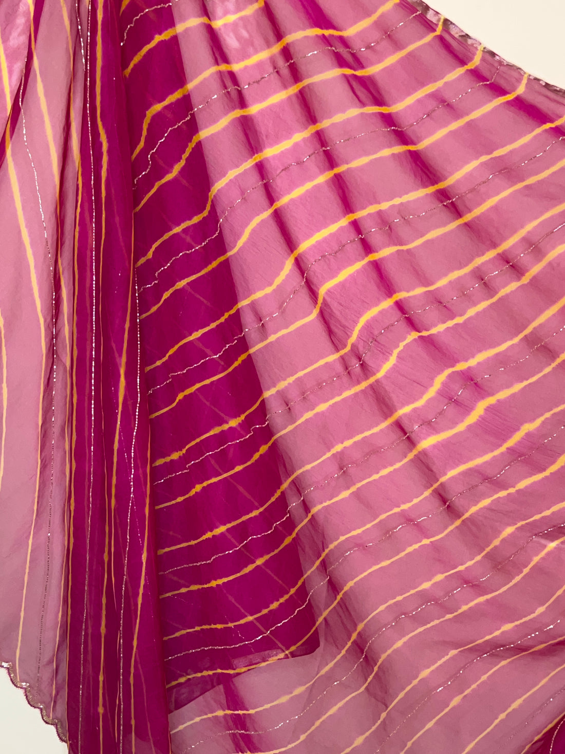 Close-up of a lightweight pink and magenta saree with soft yellow tie-dye style stripes and delicate silver shimmer lines, creating a flowing, airy look. ✨
