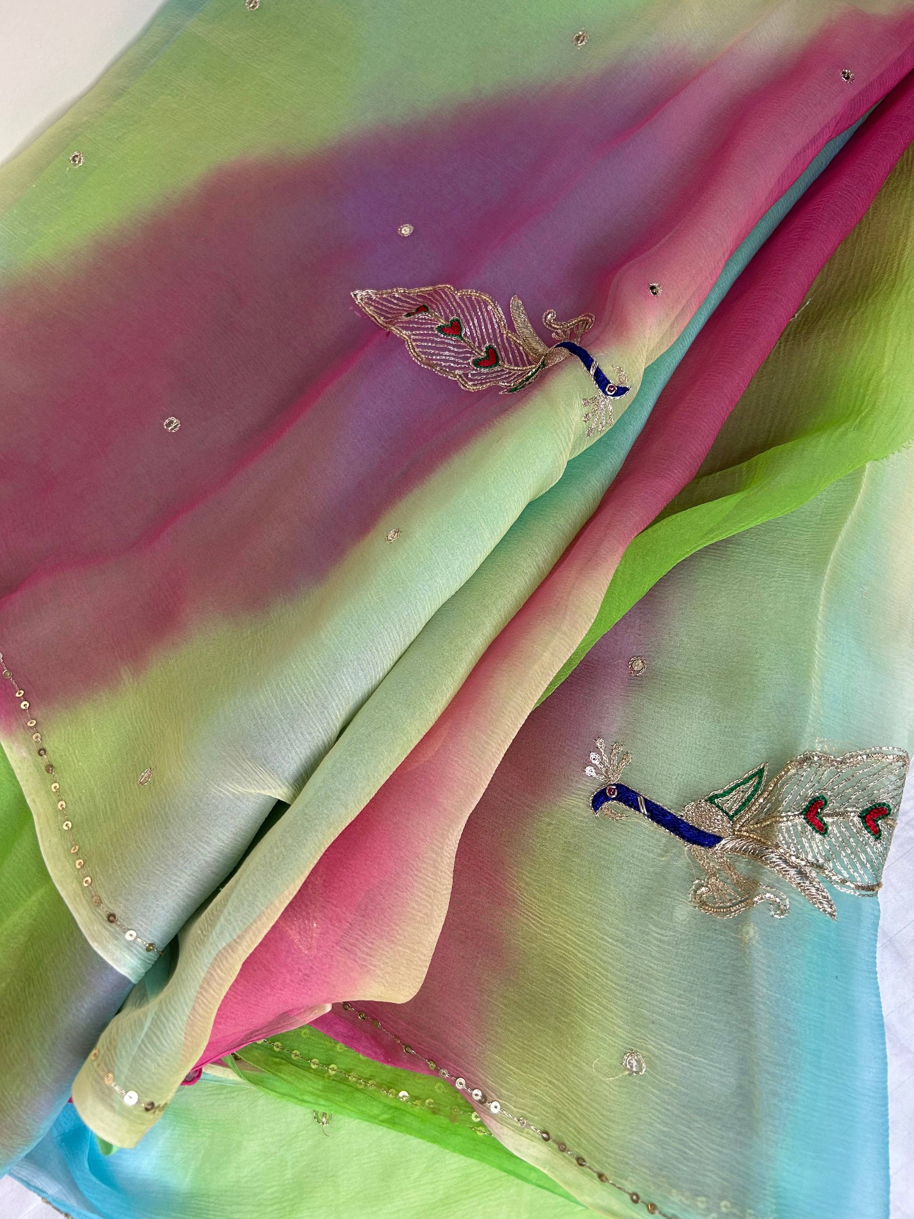 Softly draped sheer saree with a pastel gradient of mint green, sky blue, and pink, embellished with tiny crystal-like stones, a delicate sequin border, and embroidered peacock motifs in blue, silver, and red threadwork. ✨