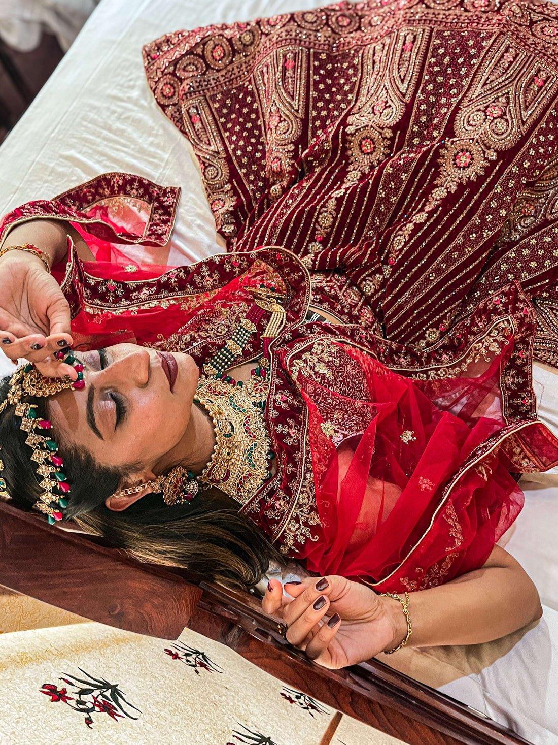 Close-up shot of Indian bridal details showing hands adorned with traditional red Chooda bangles, gold rings, and Mehndi, holding a sheer embroidered dupatta edge.