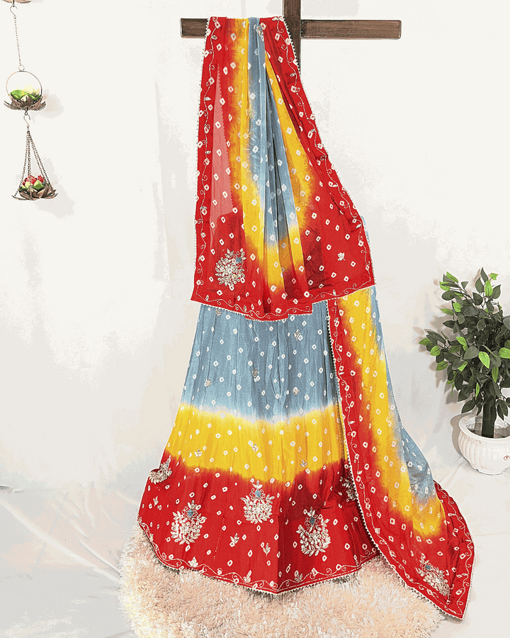 Traditional Jaipuri Bandhej Lehenga Choli in a multicolor gradient, draped on a stand. The skirt and dupatta are heavily embellished with intricate floral Gota Patti border work, suitable for weddings and Navratri festivals.