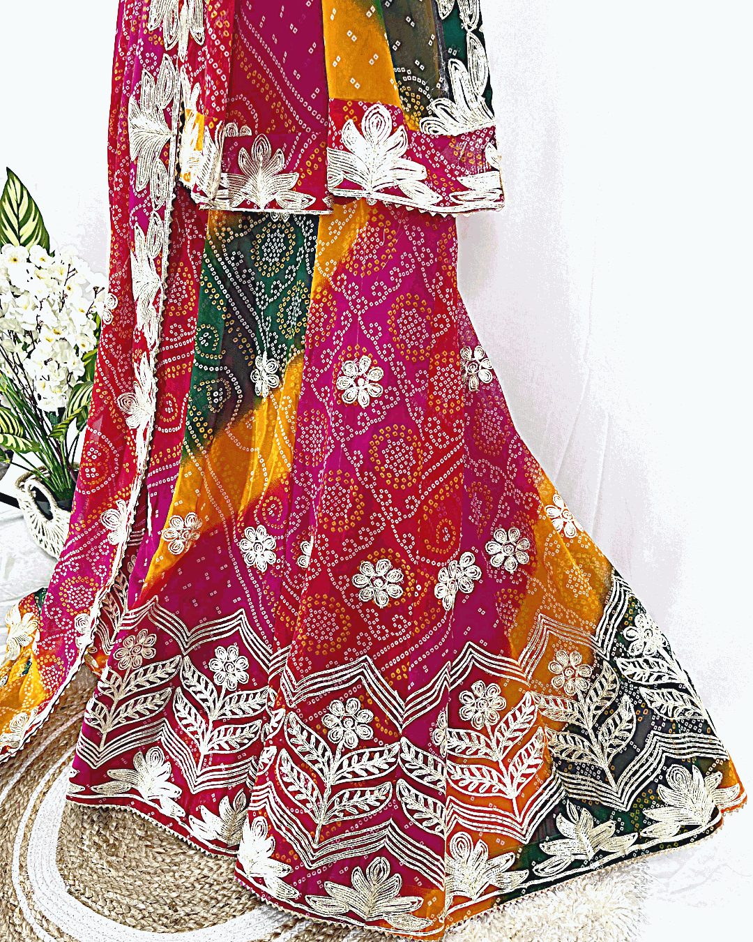 Close-up of Rajasthani Bandhani Lehenga flare featuring heavy floral Gota Patti border work and intricate Bandhej patterns on fuchsia and mustard Georgette.