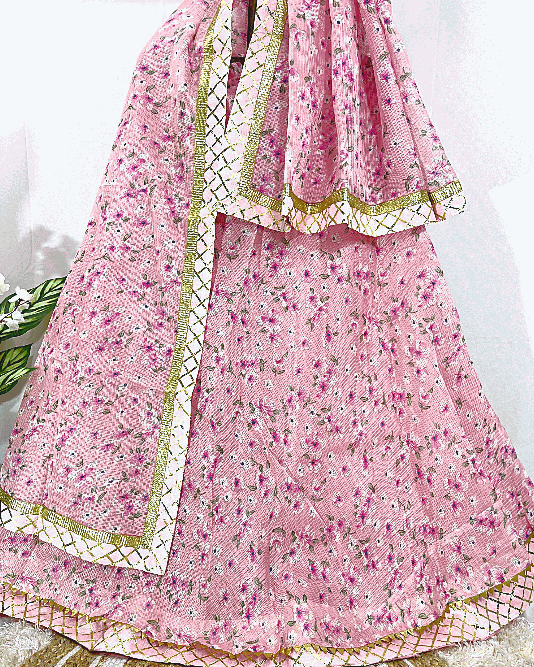 Full display of a multicolored Rajasthani Bandhani Lehenga Choli set on a wooden stand, featuring vibrant pink, orange, and green tie-dye with heavy floral Gota Patti embroidery on the border and dupatta, perfect for festive and wedding wear.