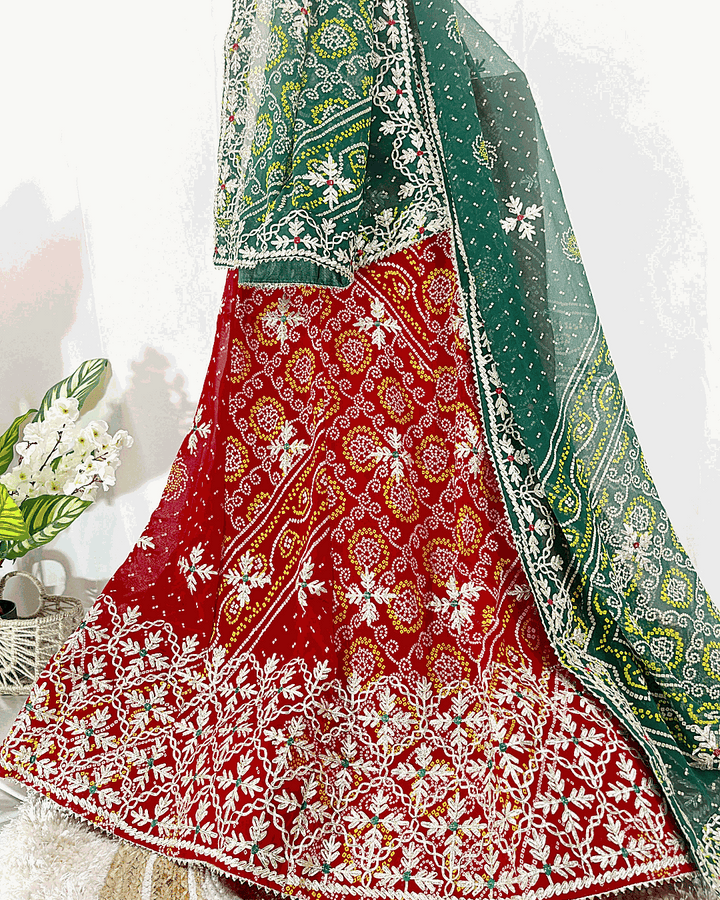 Red and Green Bandhani Lehenga Choli set with heavy silver embroidery on the border and dupatta, displayed on a wooden stand, suitable for wedding and festive wear.