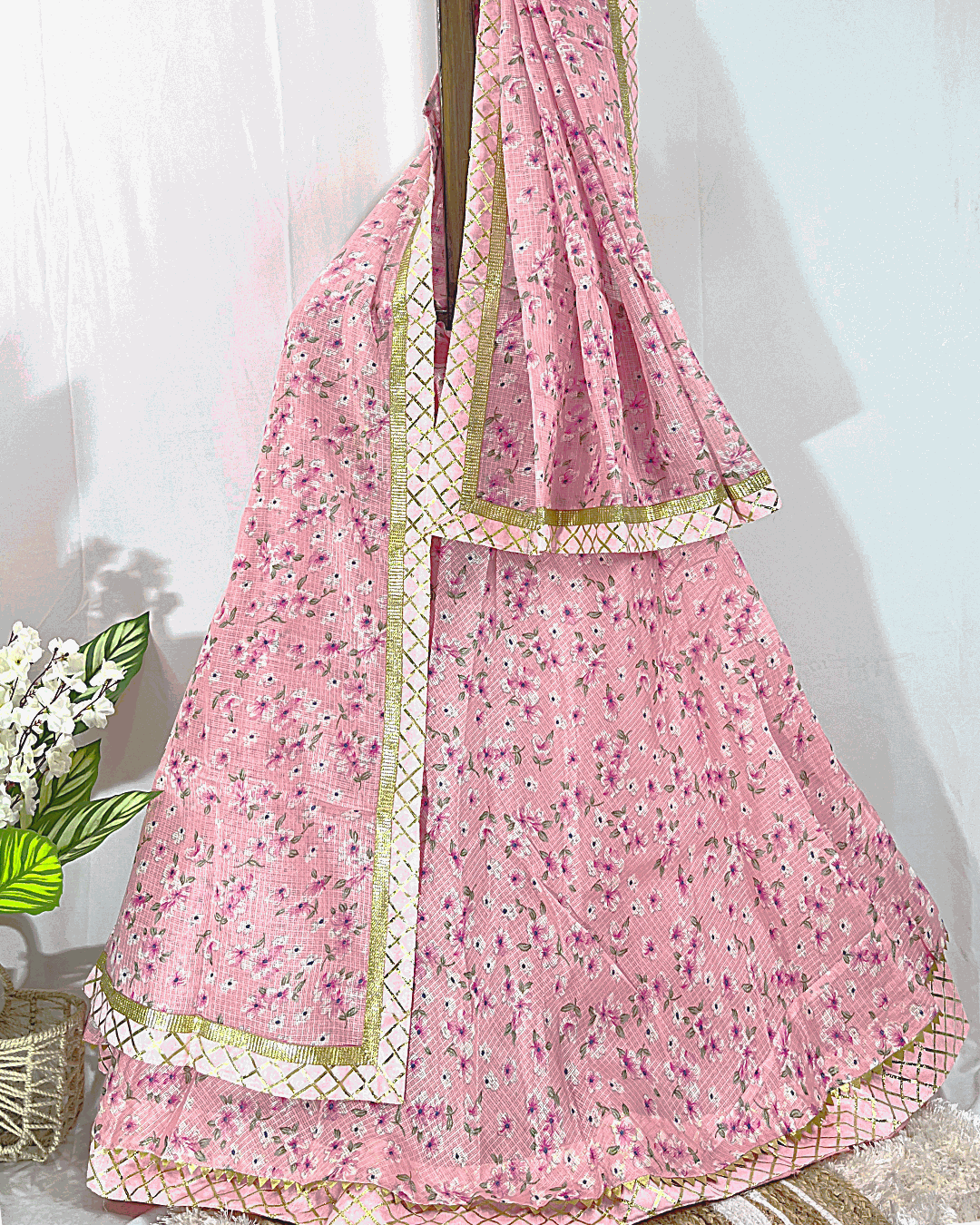 Light Pink Floral Print Lehenga Skirt and Dupatta set featuring intricate Gold Gota Patti border work, displayed on a wooden stand for festive wear.