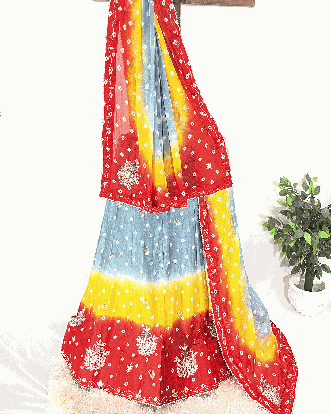 Traditional Rajasthani Bandhani Lehenga Choli in a multicolor gradient, draped on a stand. The skirt and dupatta are heavily embellished with intricate floral Gota Patti border work, suitable for weddings and Navratri festivals.